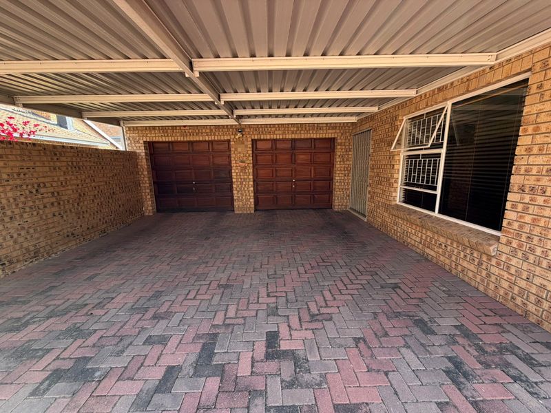 A spacious double garage featuring facebrick exterior walls, a paved driveway, and a covered carport area with a corrugated metal roof.