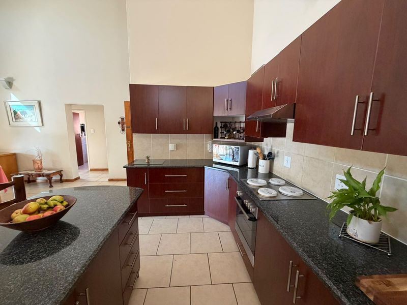 A functional kitchen featuring dark wood cabinetry, granite countertops, a central island, and built-in appliances with tiled flooring and backsplash.