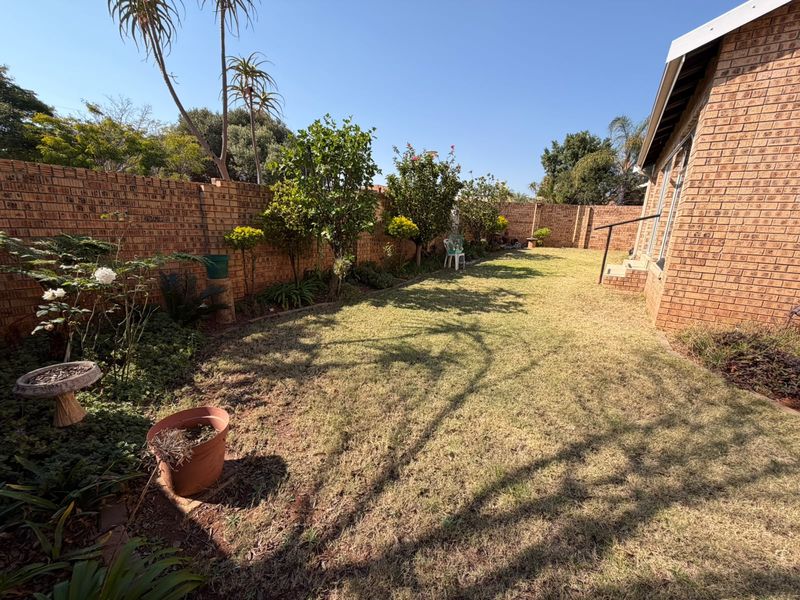 A private rear garden featuring a well-maintained lawn, established trees, and secure brick boundary walls, providing a peaceful outdoor space.
