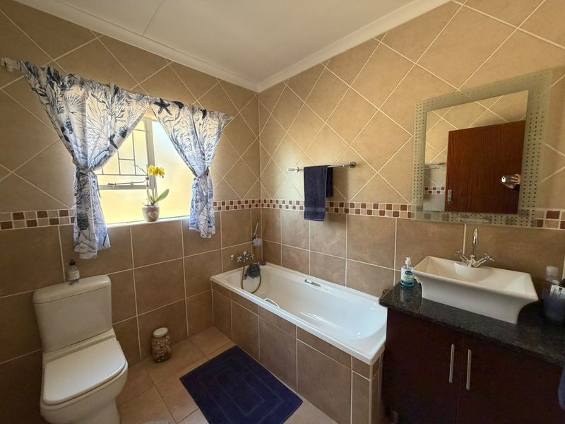 A functional bathroom featuring a built-in bathtub, a vessel sink with a vanity cabinet, and neutral ceramic wall tiling.