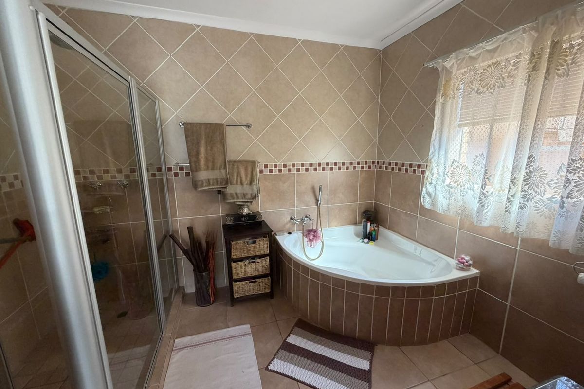 A functional bathroom featuring a corner bathtub, a separate tiled shower enclosure, and neutral wall tiling throughout.
