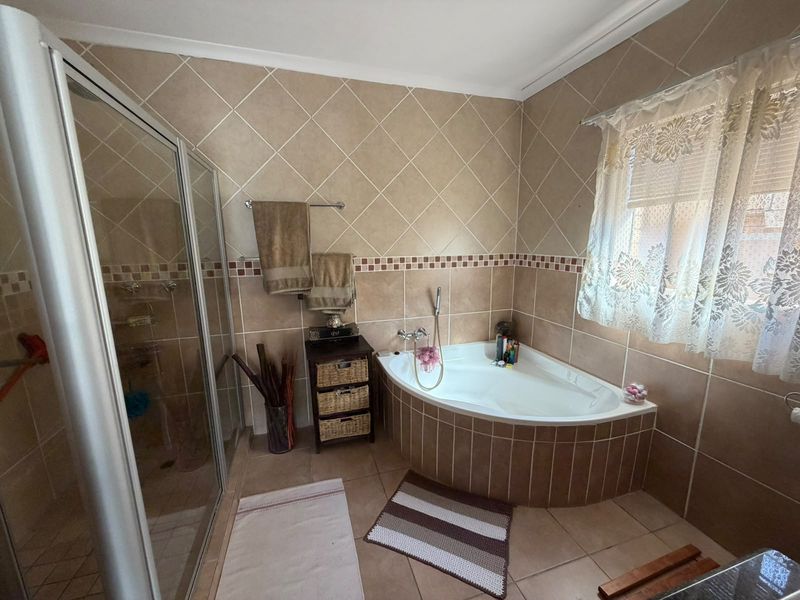 A functional bathroom featuring a corner bathtub, a separate tiled shower enclosure, and neutral wall tiling throughout.