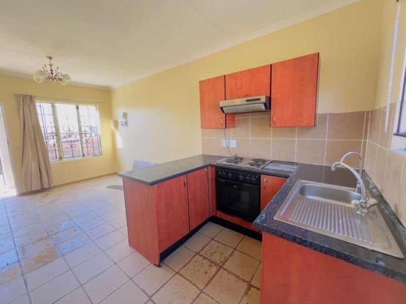 Open-plan kitchen and living area featuring built-in cabinetry, electric oven, hob, and tiled flooring. The space is vacant and ready for renovation.