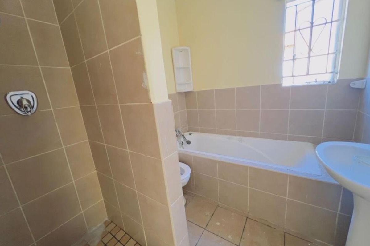A functional bathroom featuring a bathtub, separate shower area, and pedestal basin with neutral wall and floor tiling.