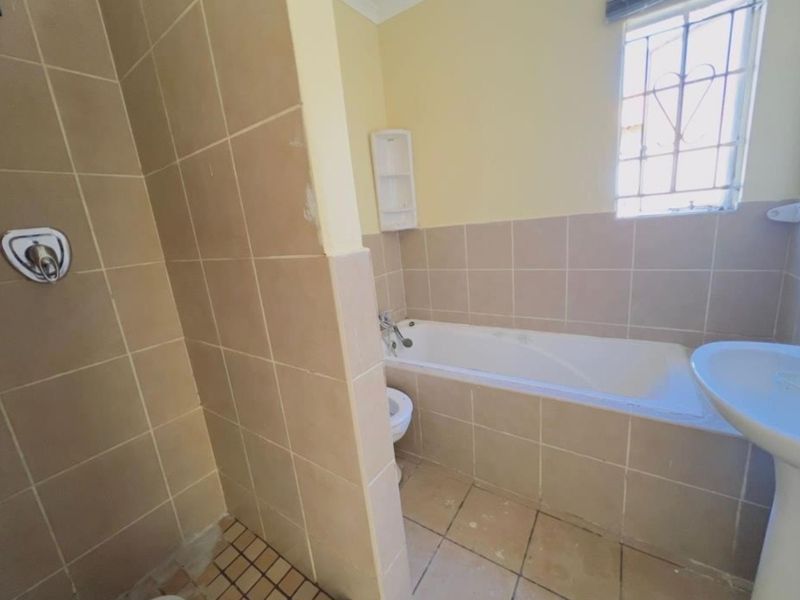 A functional bathroom featuring a bathtub, separate shower area, and pedestal basin with neutral wall and floor tiling.