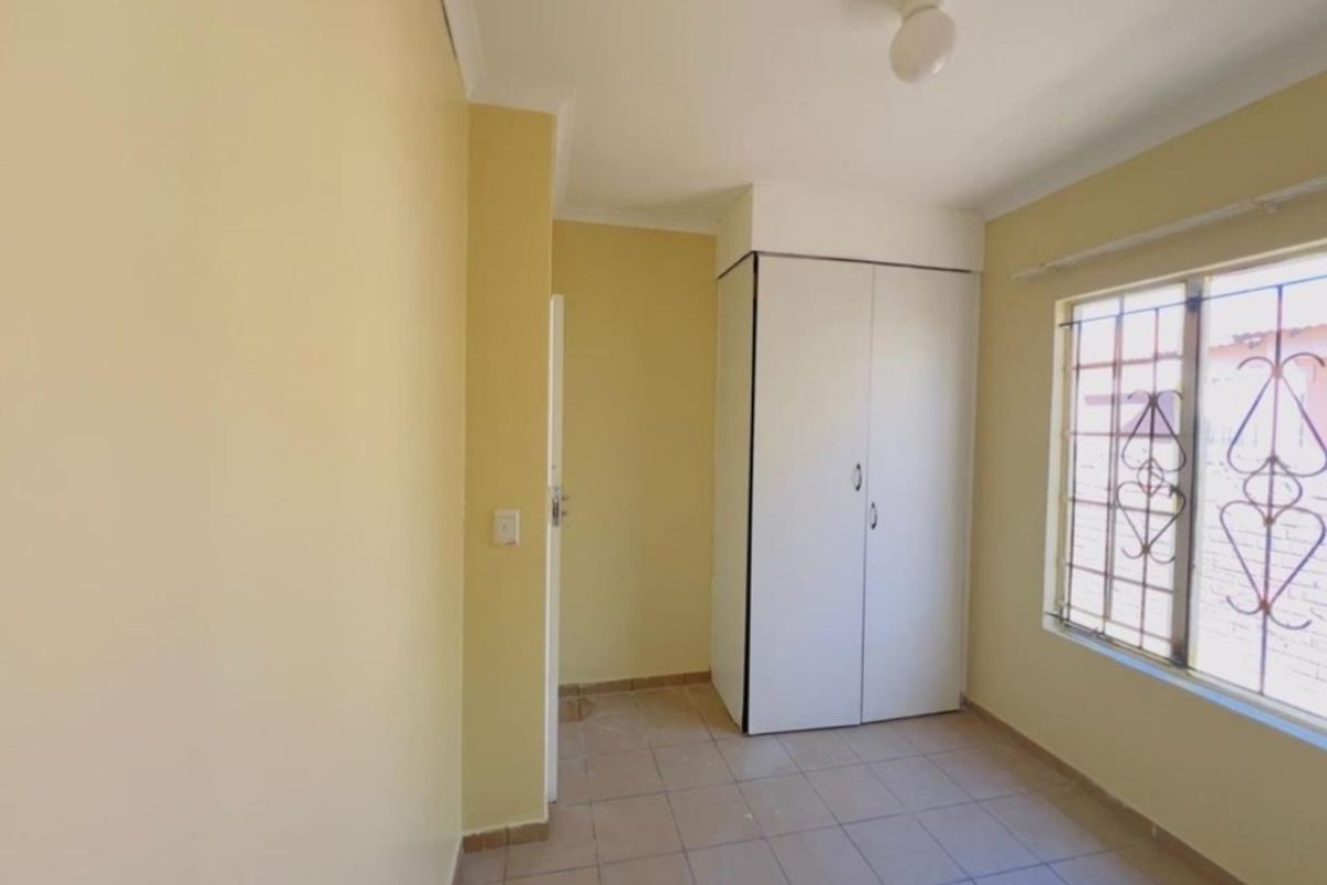 A simple, empty bedroom featuring tiled flooring, a built-in wardrobe, and a window fitted with security bars.