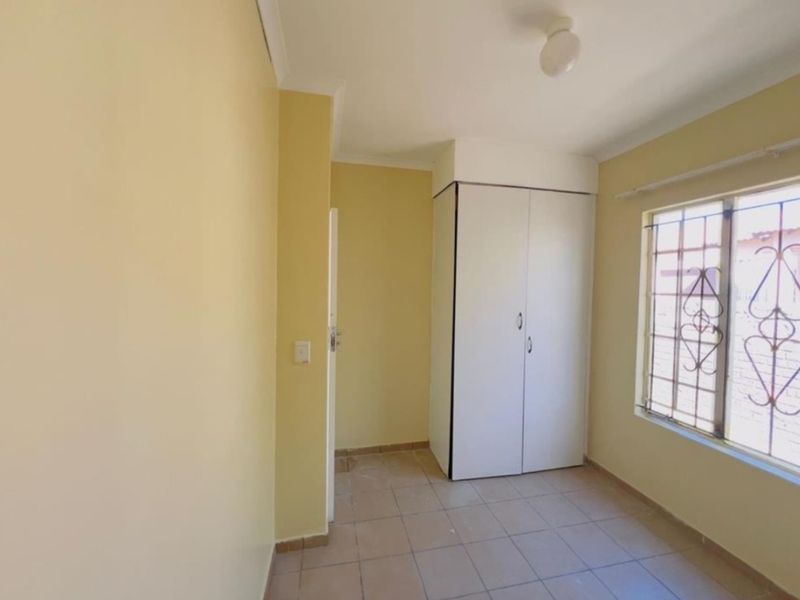 A simple, empty bedroom featuring tiled flooring, a built-in wardrobe, and a window fitted with security bars.