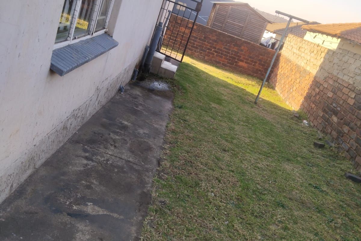 Rear exterior view of the property featuring a concrete pathway, lawn area, and brick boundary walling.