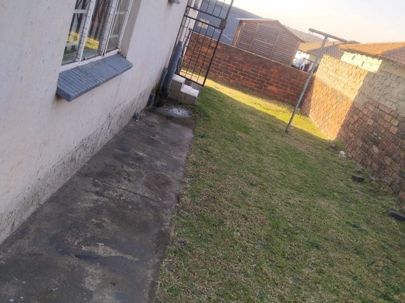 Rear exterior view of the property featuring a concrete pathway, lawn area, and brick boundary walling.
