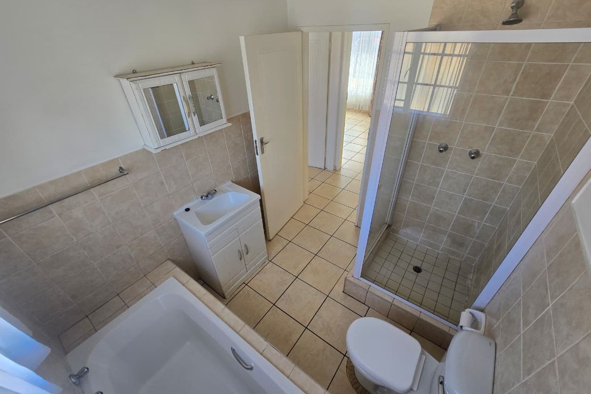 A functional bathroom featuring a bathtub, separate shower enclosure, vanity unit, and toilet with neutral tiled finishes.