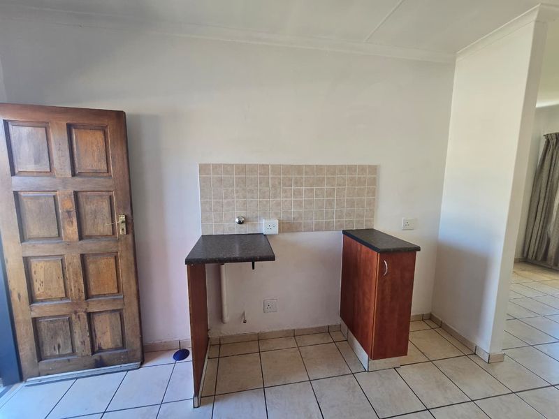 A functional laundry area featuring tiled flooring, a tiled splashback, and basic cabinetry with plumbing connections ready for appliance installation.