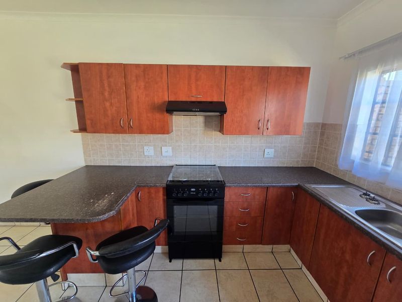 A functional kitchen featuring wood-look cabinetry, dark laminate countertops, a freestanding stove with extractor fan, and tiled flooring.