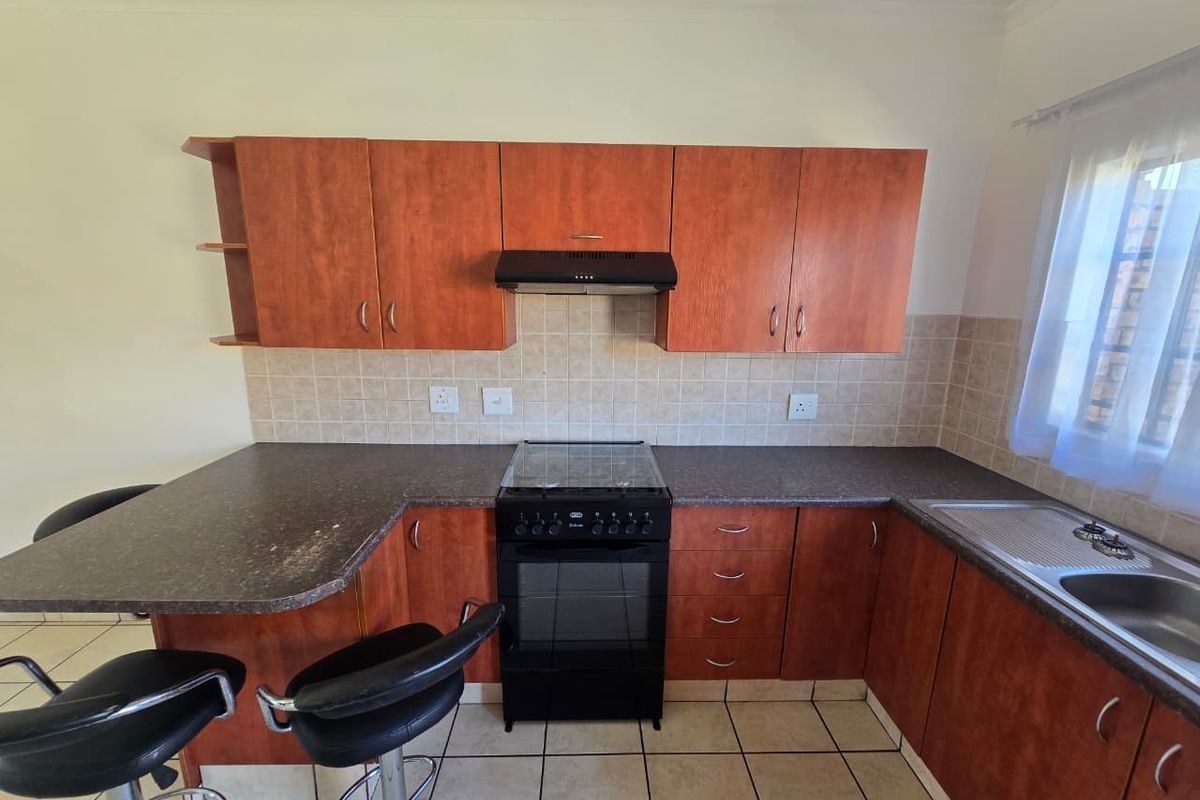 A functional kitchen featuring wood-look cabinetry, dark laminate countertops, a freestanding stove with extractor fan, and tiled flooring.