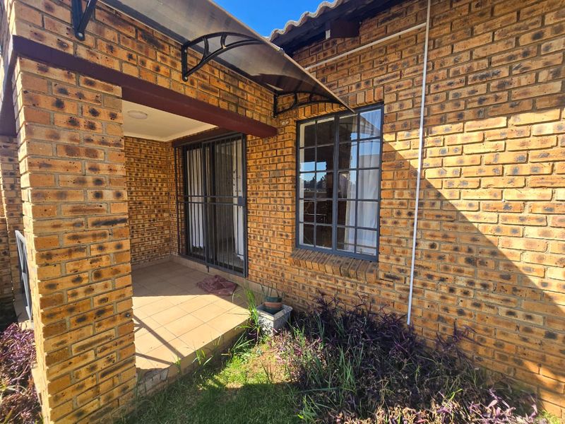 A covered face brick patio area featuring tiled flooring, a security gate, and a protective awning, providing a functional outdoor space.