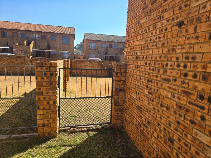 A view of the rear exterior area featuring face brick walls and a metal gate, providing access to the garden space.