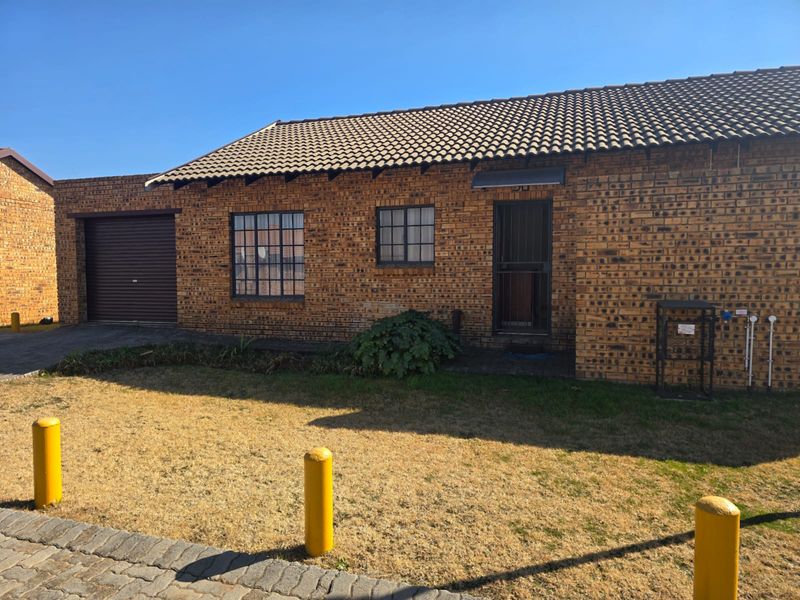 Front elevation of a facebrick townhouse featuring a tiled roof, integrated garage with roller door, and secure entrance.