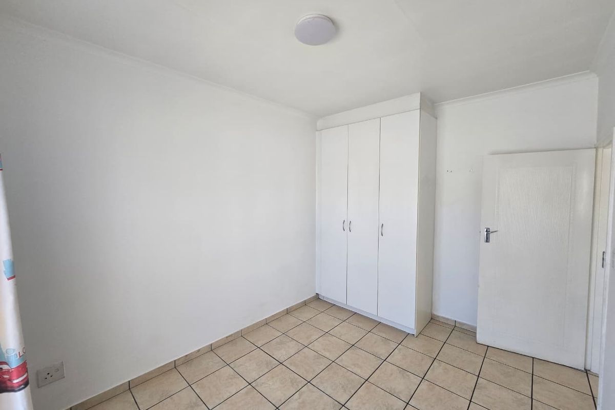 A clean, empty bedroom featuring neutral tiled flooring and a white built-in wardrobe, offering a blank canvas for personalization.