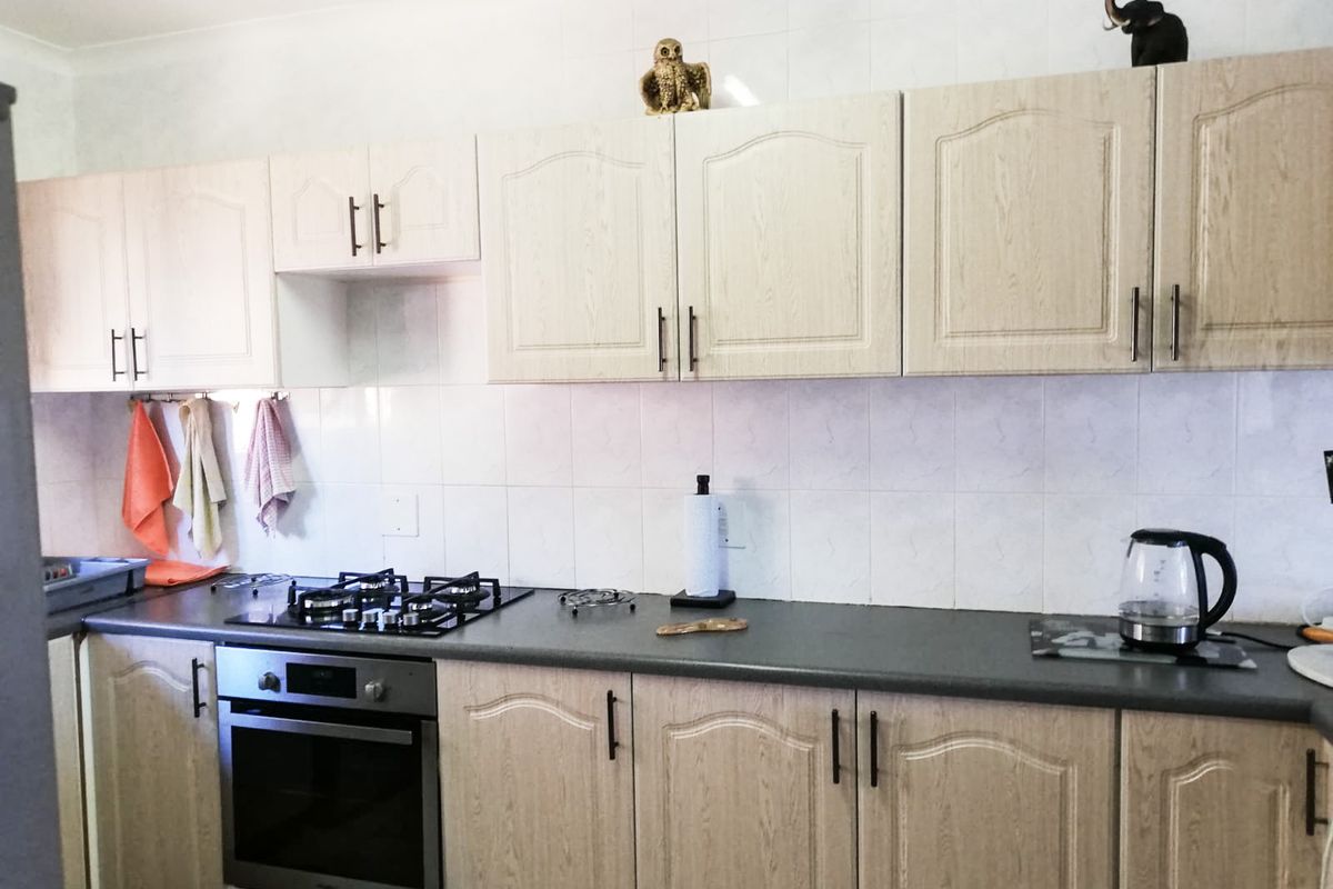 A functional kitchen featuring light wood-grain cabinetry, dark laminate countertops, a built-in oven, and a gas hob with a tiled backsplash.