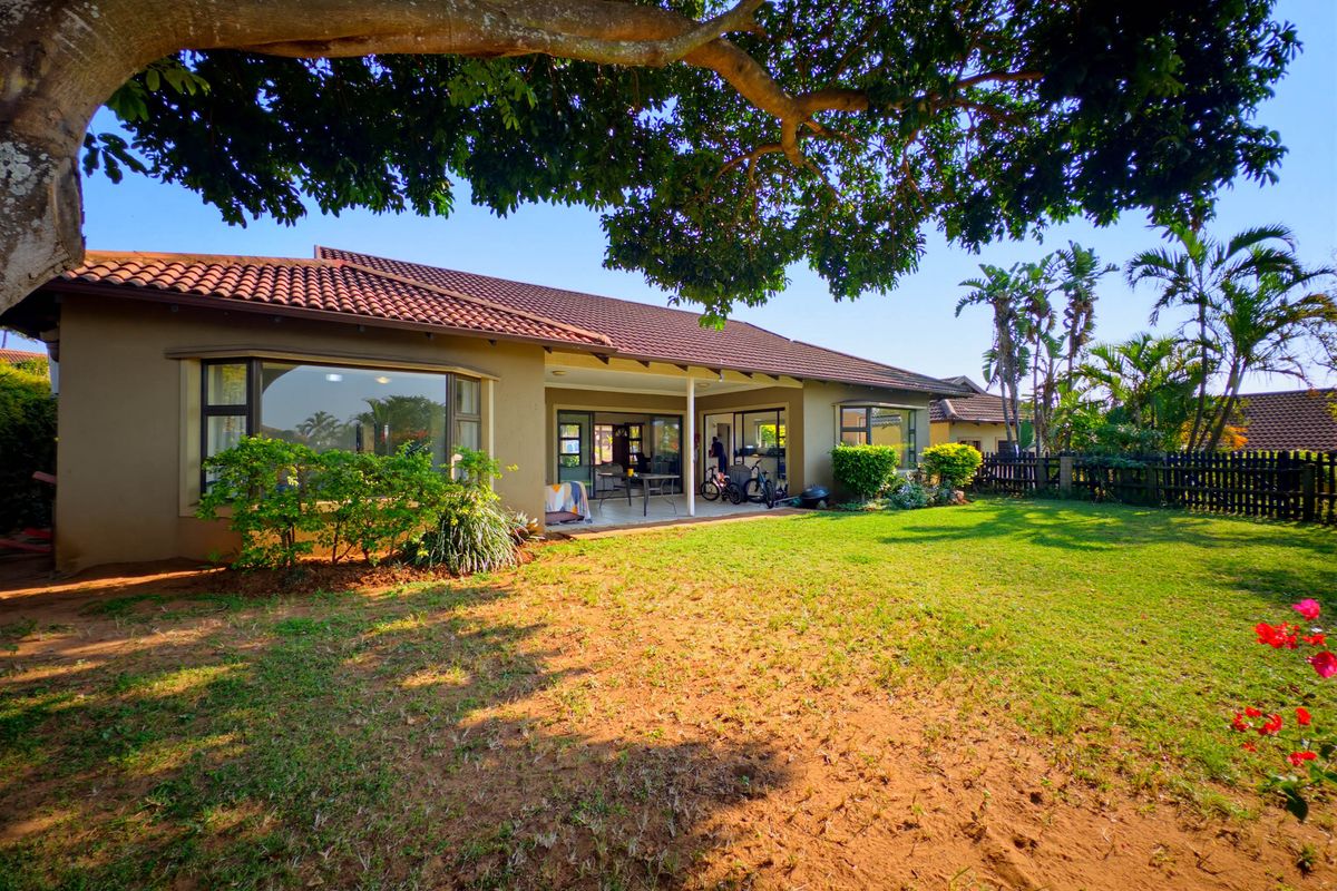 Rear view of the house featuring a covered patio, bay windows, terracotta roof tiles, and a spacious garden with mature trees.