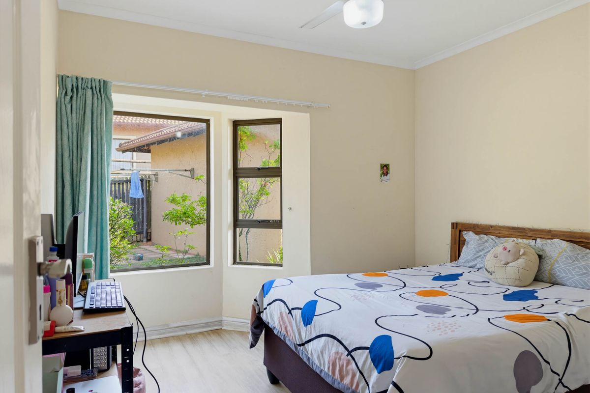 A bedroom featuring a ceiling fan, laminate flooring, and a bay window overlooking the rear garden area.