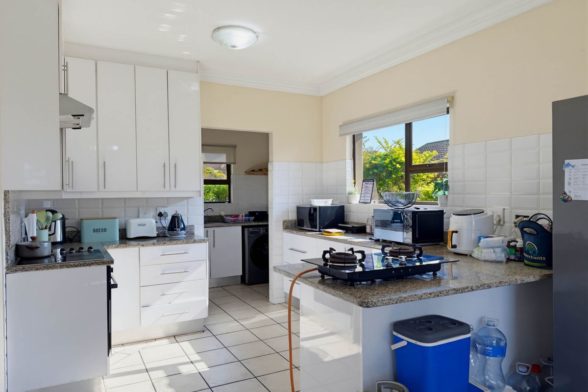 A functional kitchen featuring white cabinetry, granite countertops, tiled backsplash, and ceramic tile flooring, with an adjoining scullery area visible.