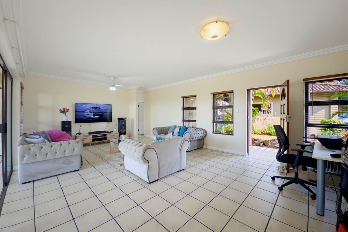 Spacious living room featuring tiled flooring, ceiling fan, and direct access to the exterior through a sliding glass door and side entrance.
