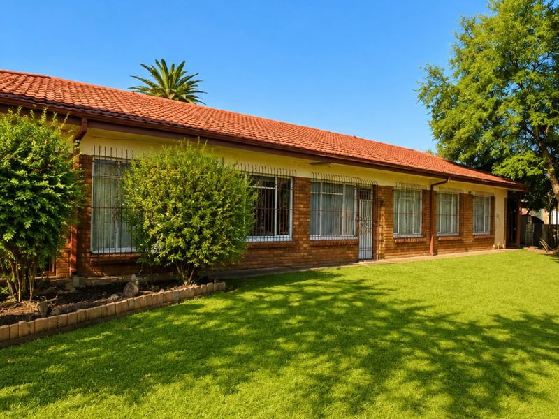 A well-maintained single-story brick house featuring a tiled roof, security bars on windows, and a spacious front lawn.