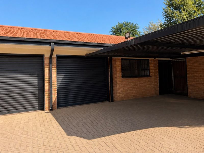 A well-maintained exterior view featuring a double garage with roller doors, an attached carport, and a paved driveway.