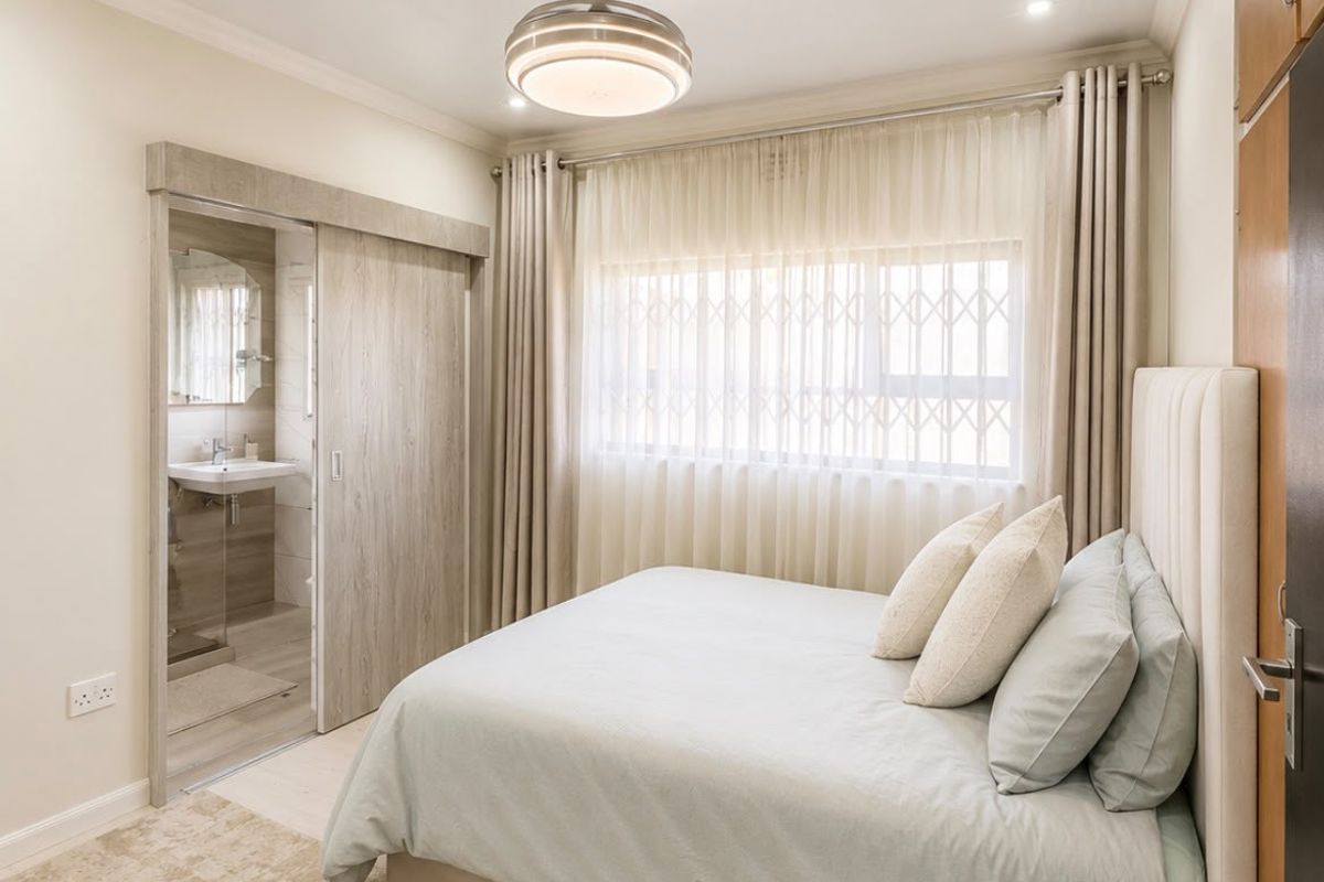 A well-maintained bedroom featuring a sliding door leading to an en-suite bathroom, built-in cupboards, and a modern ceiling fan.