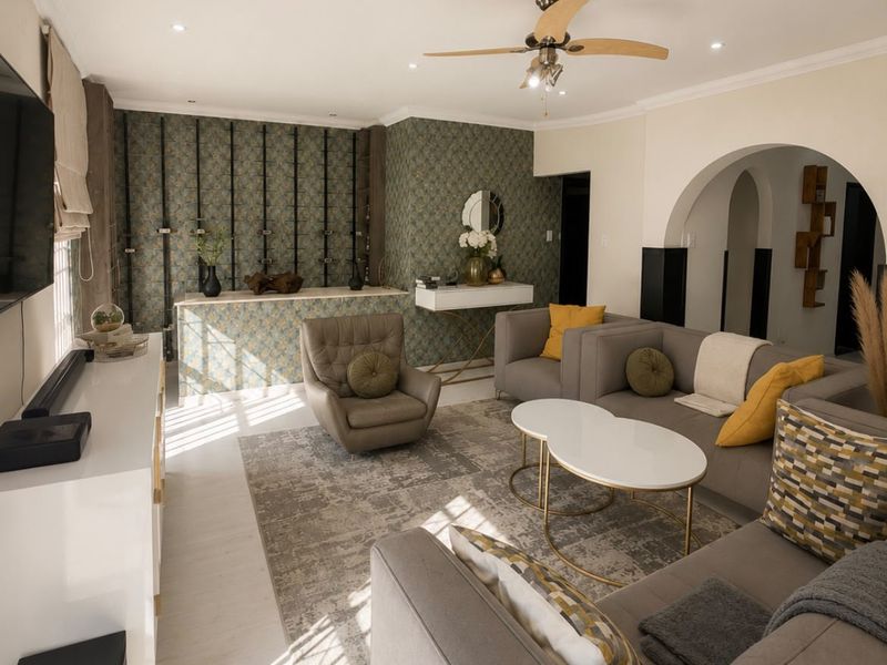 A well-lit living room featuring a ceiling fan, decorative wallpaper accent wall, and a classic architectural archway leading to adjacent spaces.