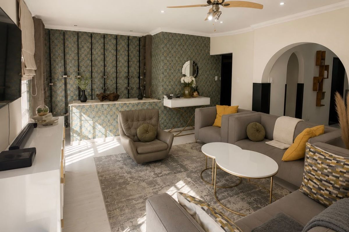 A well-lit living room featuring a ceiling fan, decorative wallpaper accent wall, and a classic architectural archway leading to adjacent spaces.