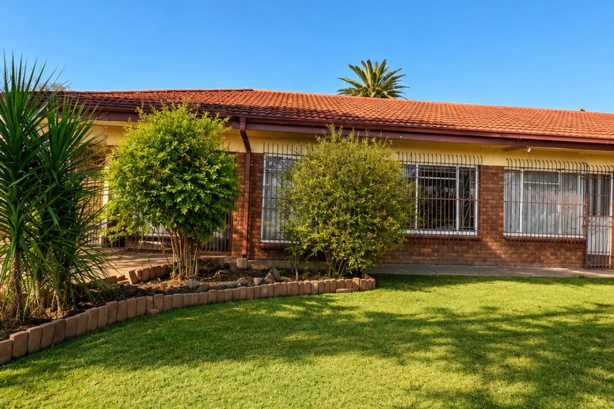 A view of the rear facade featuring a terracotta tiled roof, face brick exterior, and security-fitted windows overlooking a well-maintained lawn.