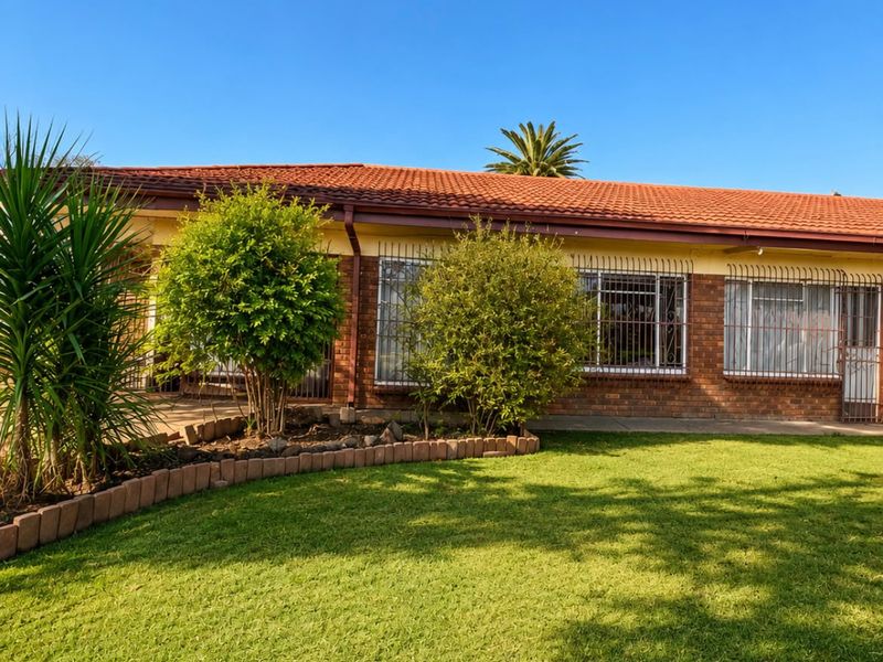 A view of the rear facade featuring a terracotta tiled roof, face brick exterior, and security-fitted windows overlooking a well-maintained lawn.