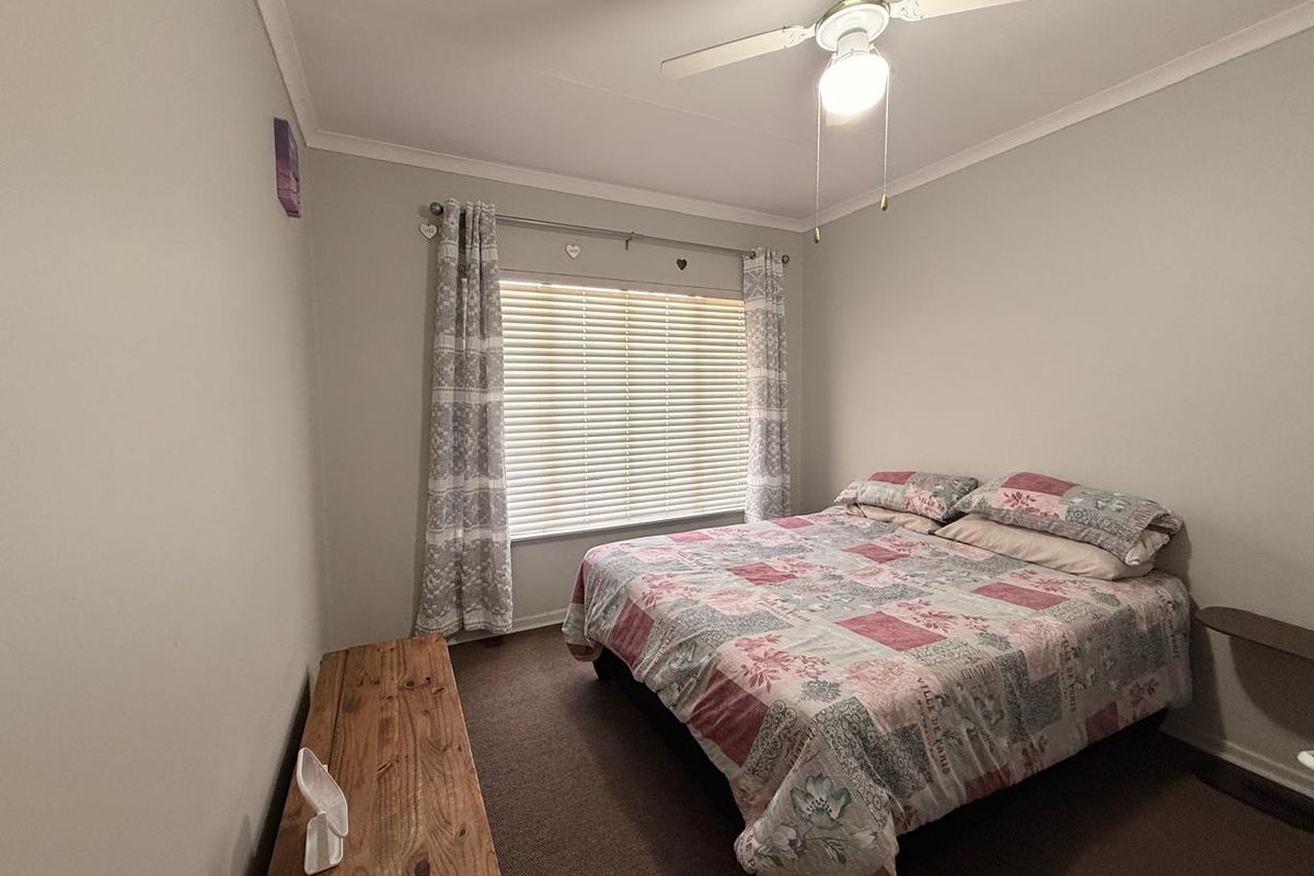 A functional bedroom featuring carpeted flooring, a ceiling fan, and venetian blinds, providing a neutral space ready for personalization.