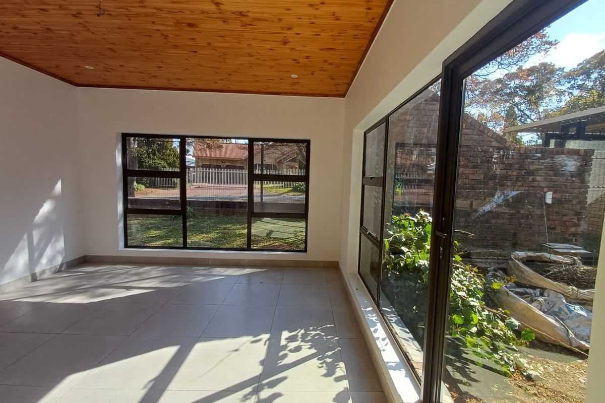 A bright, empty living area featuring large windows, a timber-clad ceiling, and neutral tiled flooring, offering a clean canvas for interior design.