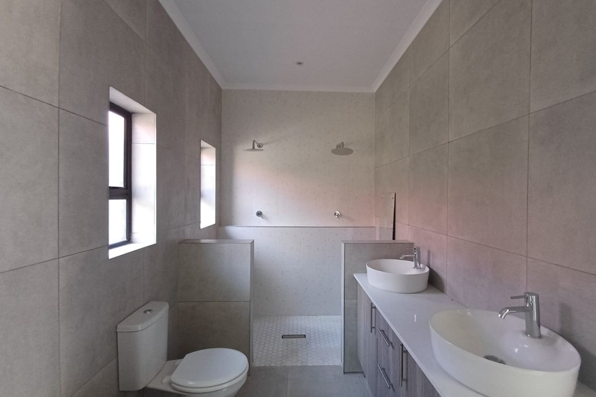 Modern bathroom featuring a double vanity with vessel sinks, a spacious walk-in shower with dual shower heads, and contemporary floor-to-ceiling tiling.