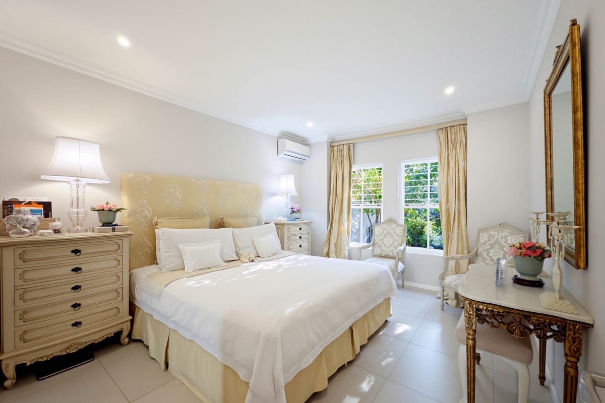 A well-maintained bedroom featuring tiled flooring, recessed downlighting, and a wall-mounted split-system air conditioning unit.