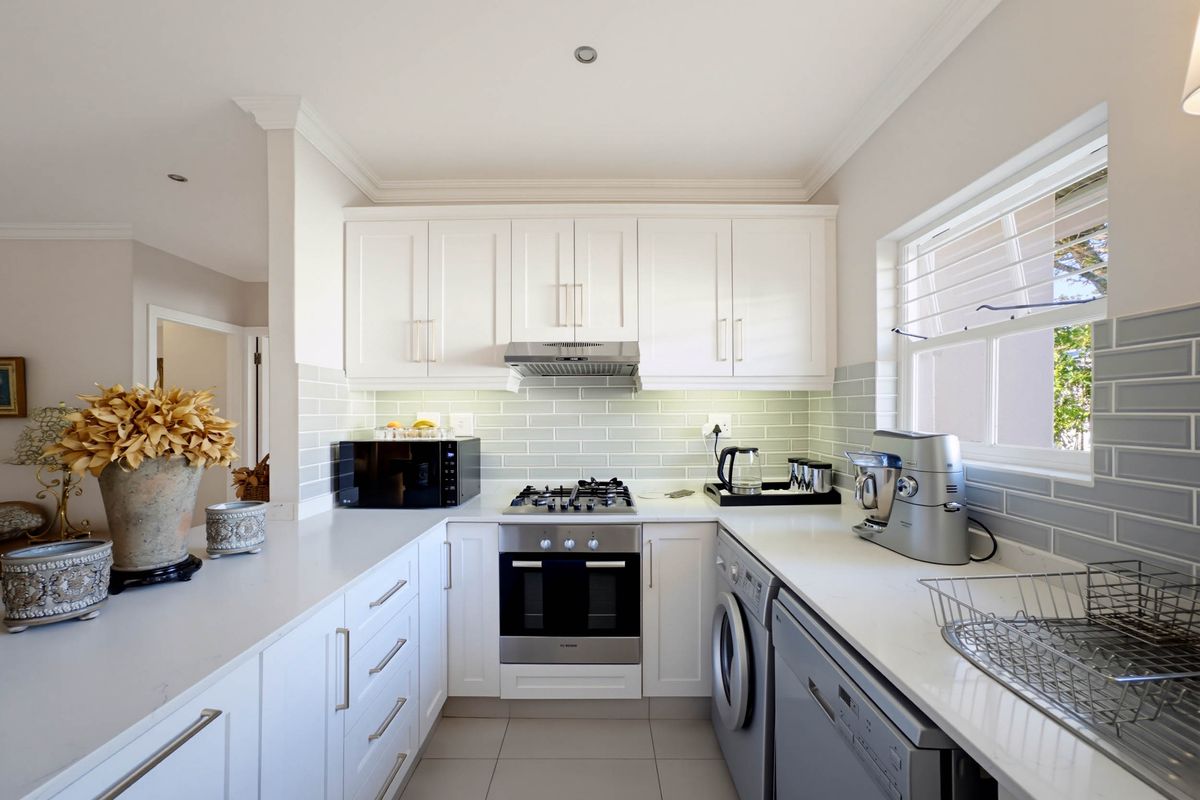 Modern kitchen featuring white cabinetry, stone countertops, subway tile backsplash, gas hob, built-in oven, and integrated laundry facilities.