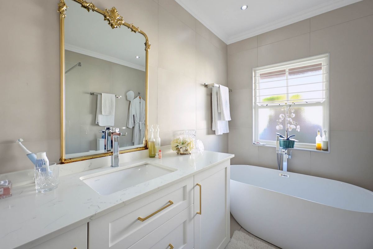 Modern bathroom featuring a sleek freestanding bathtub, a vanity with quartz countertop, and elegant gold-toned hardware against neutral tiled walls.