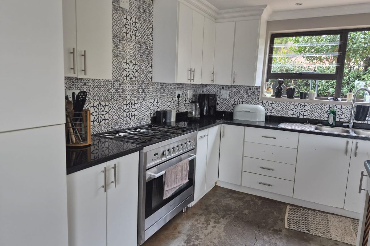 Modern kitchen featuring white cabinetry, black granite countertops, a striking patterned tile backsplash, gas stove, and durable concrete flooring.