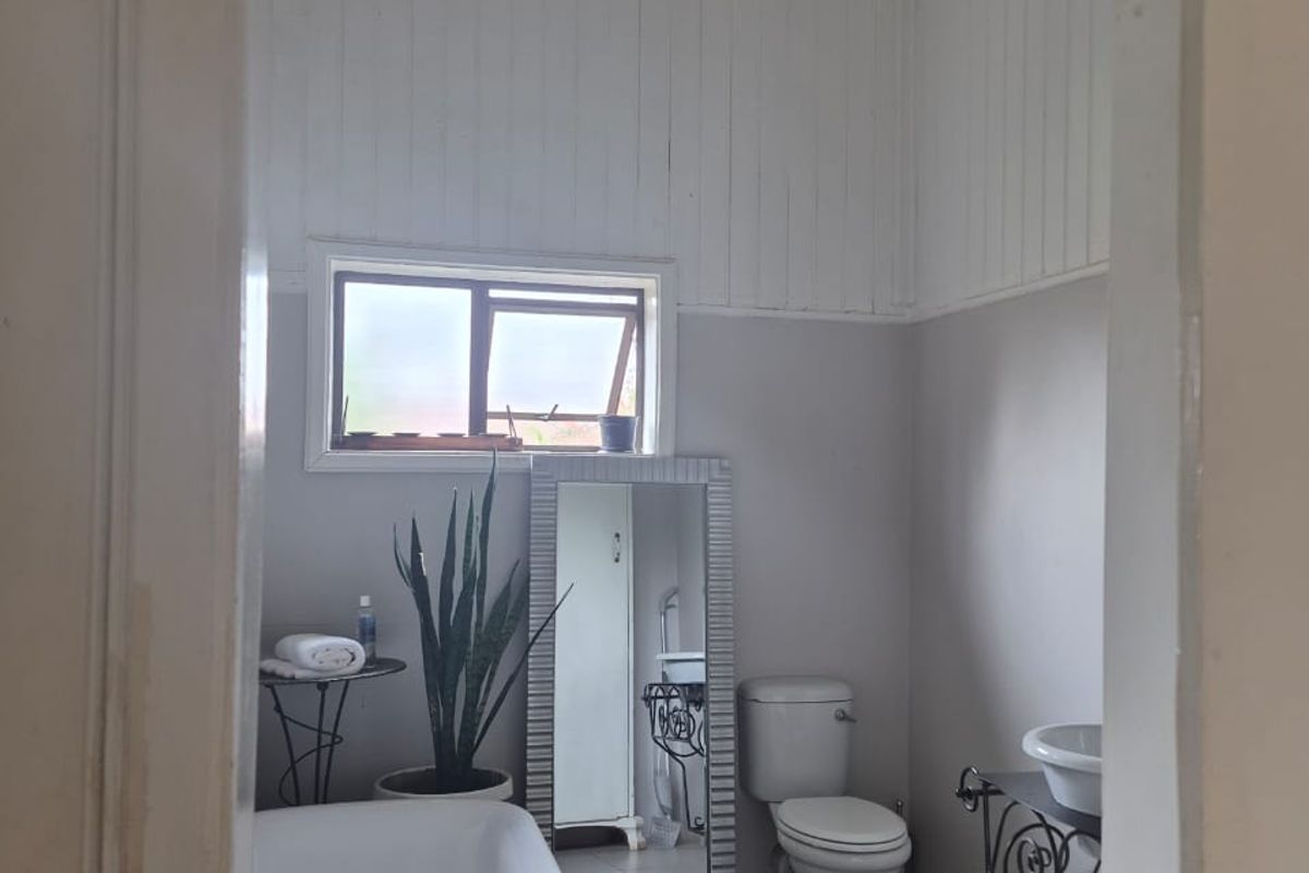 A functional bathroom featuring a freestanding bathtub, toilet, pedestal sink, and high timber-panelled ceilings with neutral wall finishes.