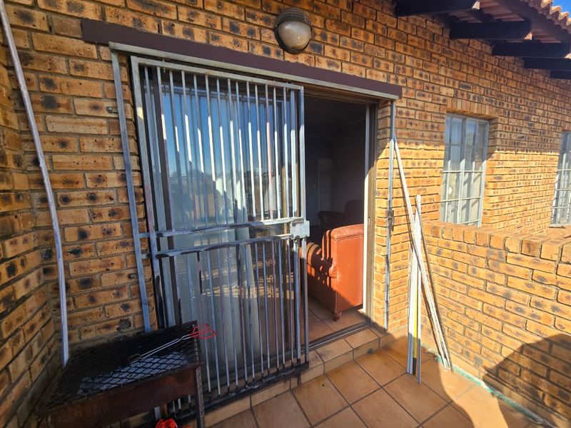 A covered patio area featuring exposed brick walls, tiled flooring, and a secure metal gate leading into the interior living space.