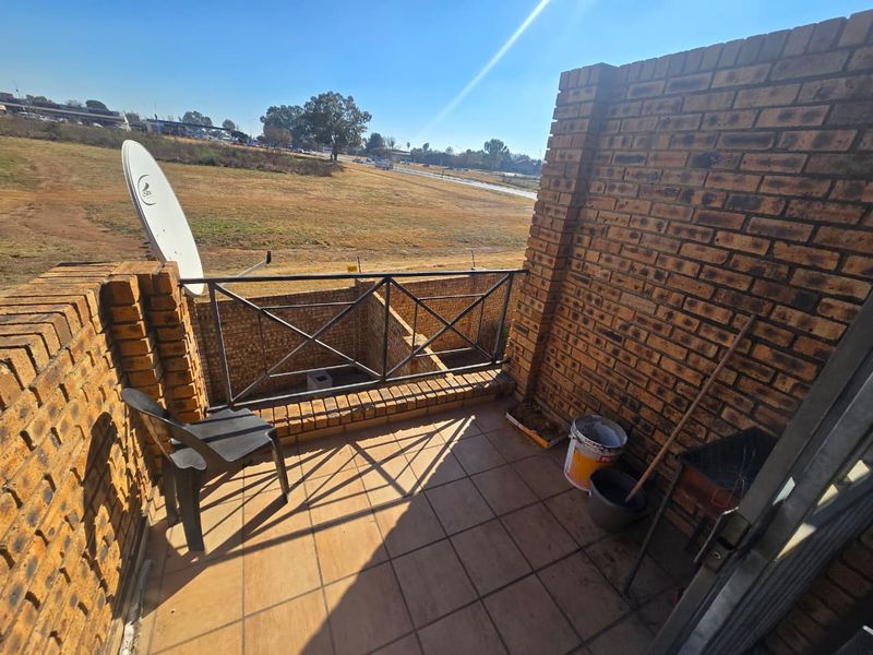 An open-air balcony featuring face brick walls, tiled flooring, and a metal balustrade, offering an elevated view of the surrounding landscape.