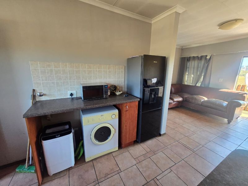 Open-plan living area featuring tiled flooring, a functional kitchen prep space with tiled splashback, and direct access to the adjacent lounge area.
