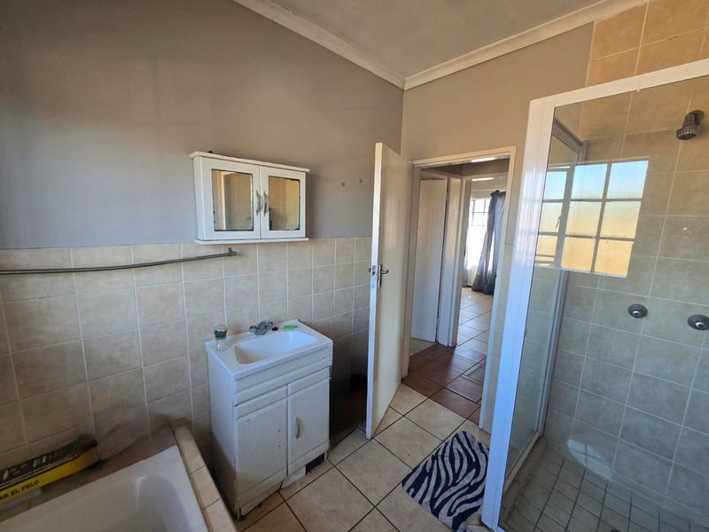 A functional bathroom featuring a shower enclosure, bathtub, and vanity basin with wall-mounted storage, requiring cosmetic updates to modernize the space.