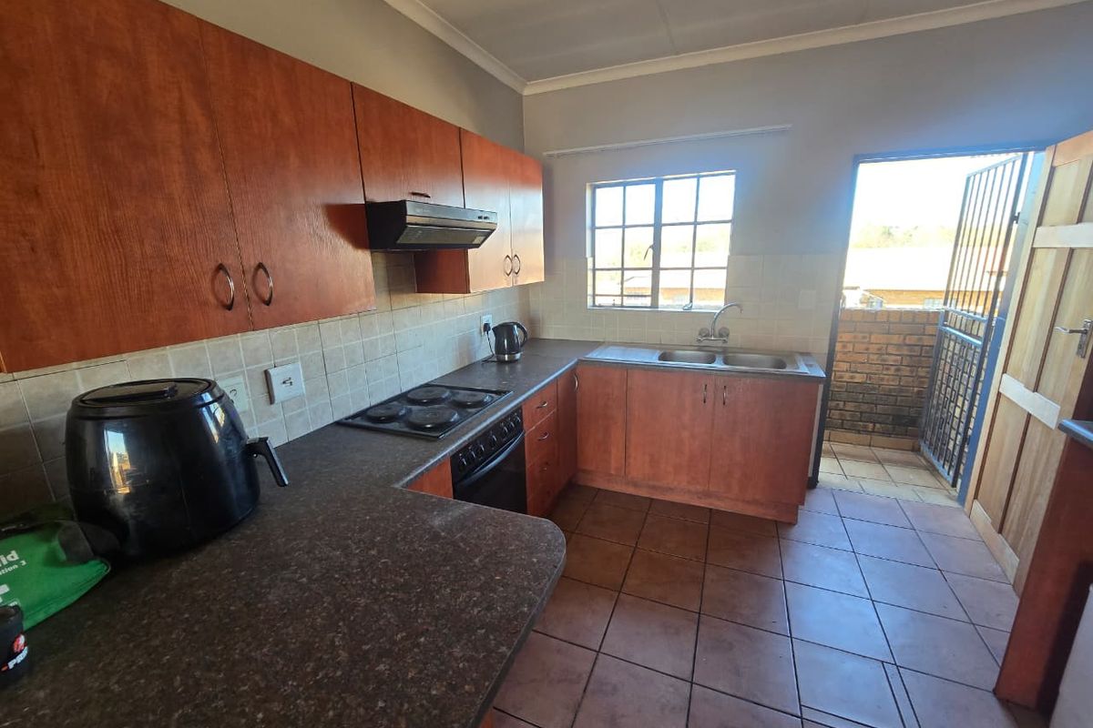 Functional kitchen featuring wood-look cabinetry, laminate countertops, built-in oven with hob, and direct access to an outdoor area through a security gate.