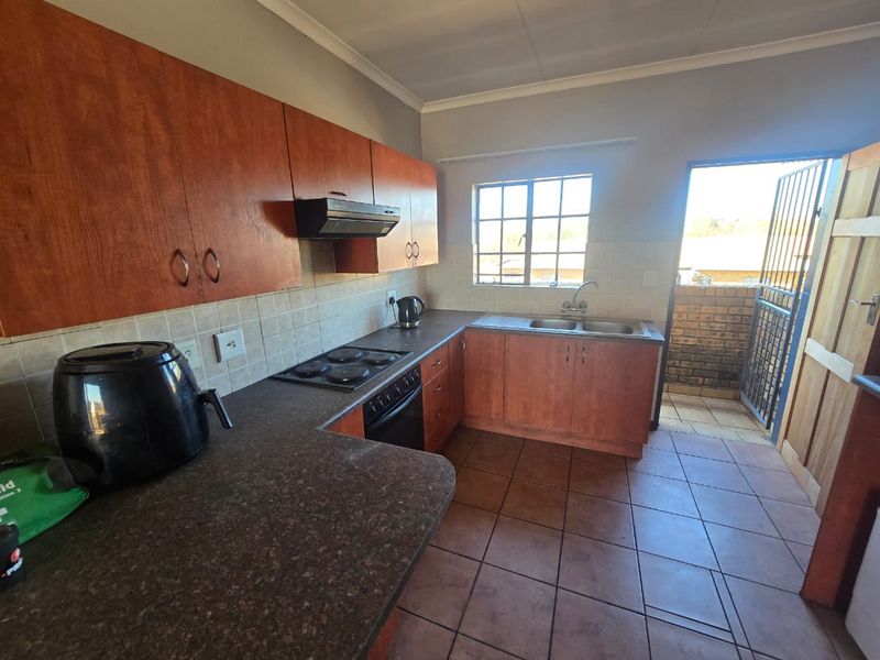 Functional kitchen featuring wood-look cabinetry, laminate countertops, built-in oven with hob, and direct access to an outdoor area through a security gate.