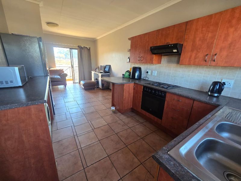 Open-plan kitchen and living area featuring wood-finish cabinetry, tiled flooring, and direct access to a balcony through sliding glass doors.