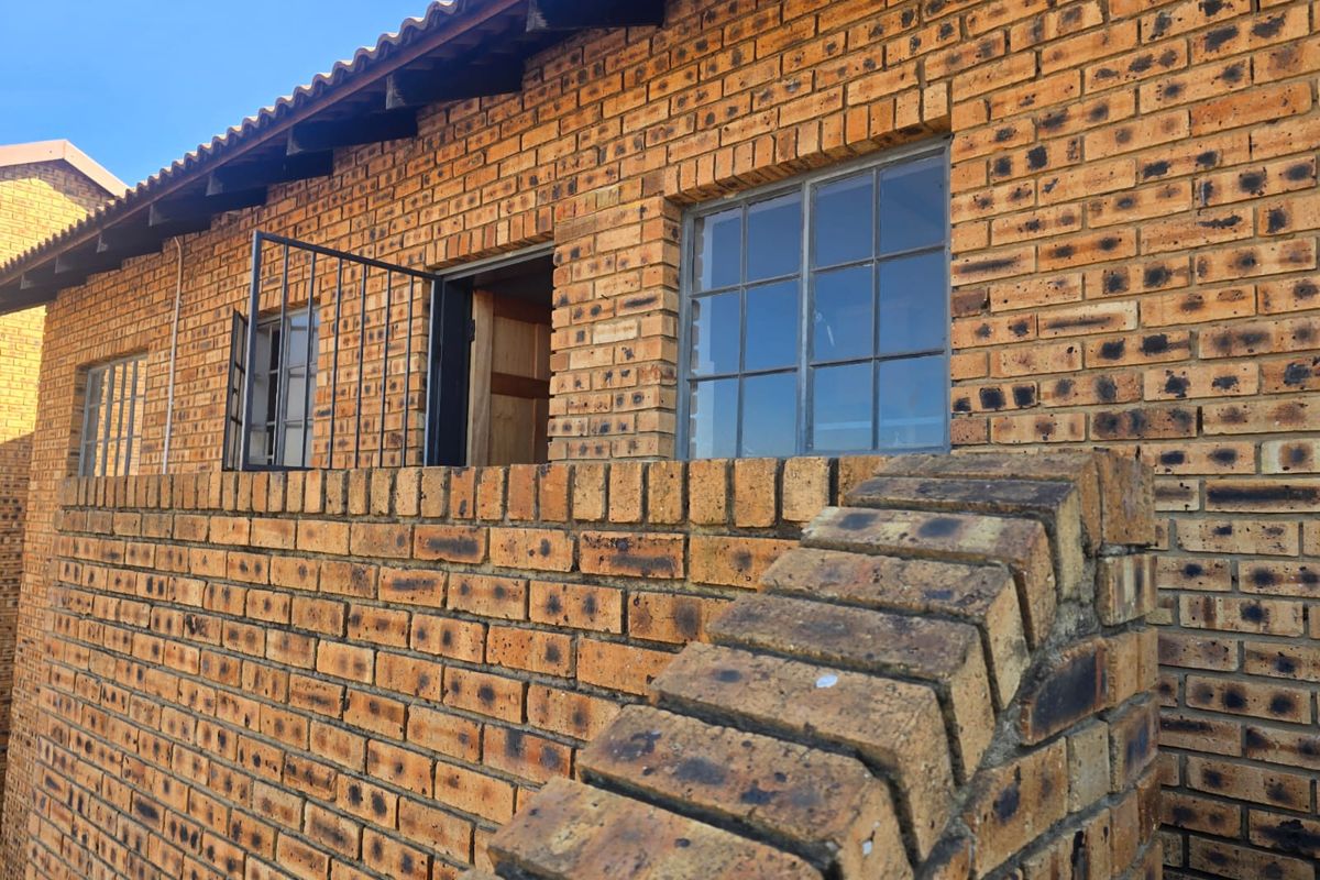 Exterior view of the townhouse featuring a classic face brick facade, tiled roof, and steel-framed windows with a low brick boundary wall.