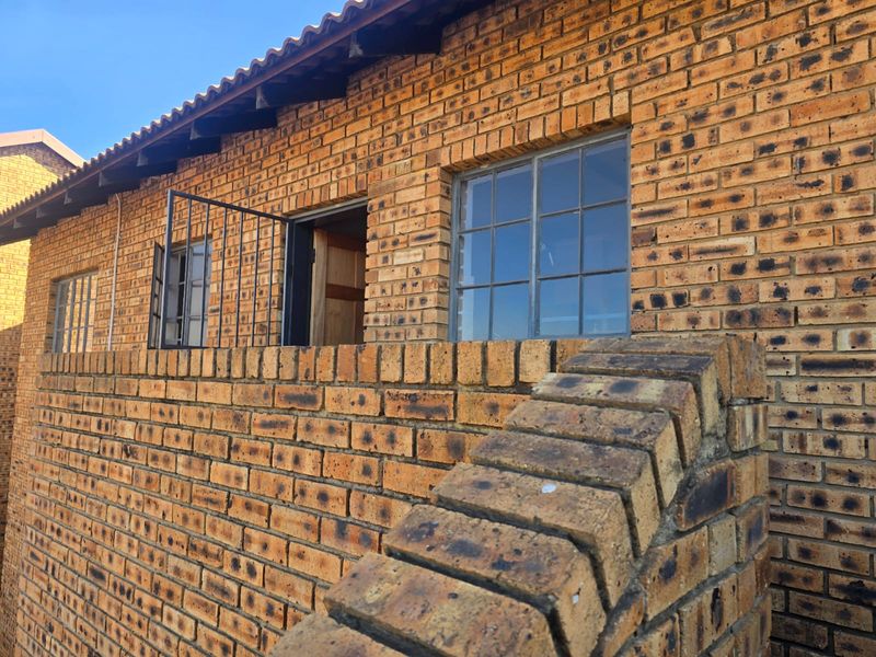 Exterior view of the townhouse featuring a classic face brick facade, tiled roof, and steel-framed windows with a low brick boundary wall.